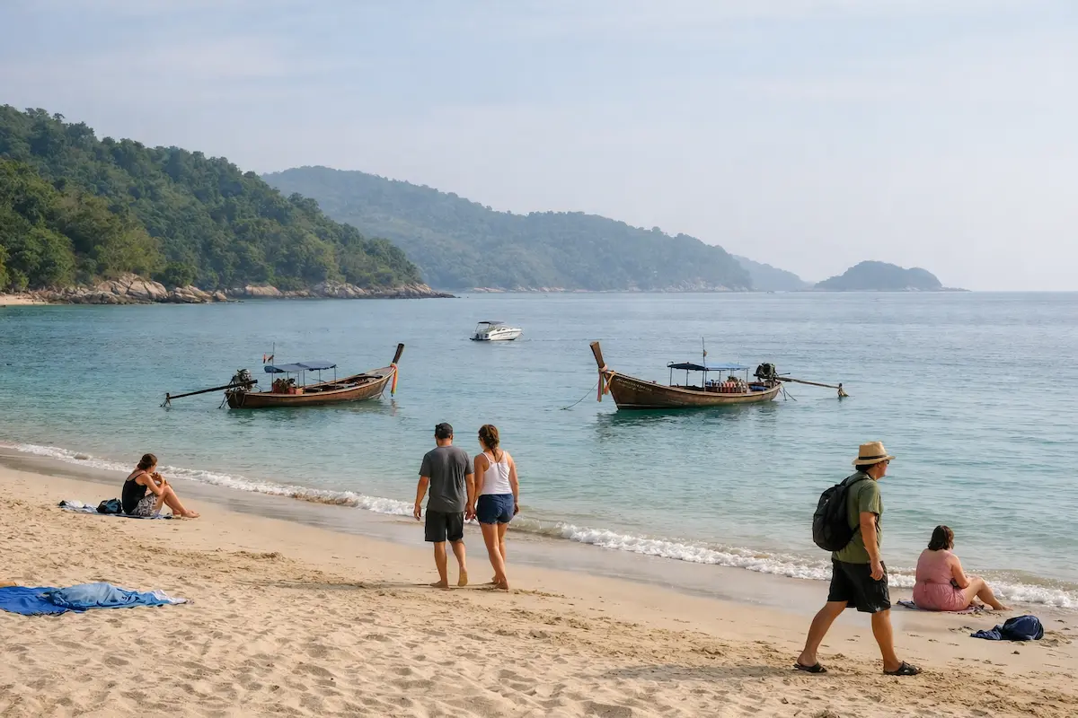Phuket travel itinerary beach scene with longtail boats and tourists walking along the shoreline