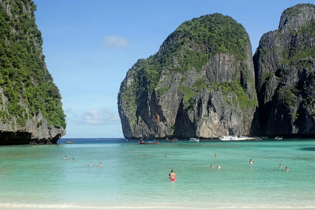 Realistic Phuket beach scene with travellers in shallow water near limestone cliffs, showing natural travel conditions in a Phuket trip